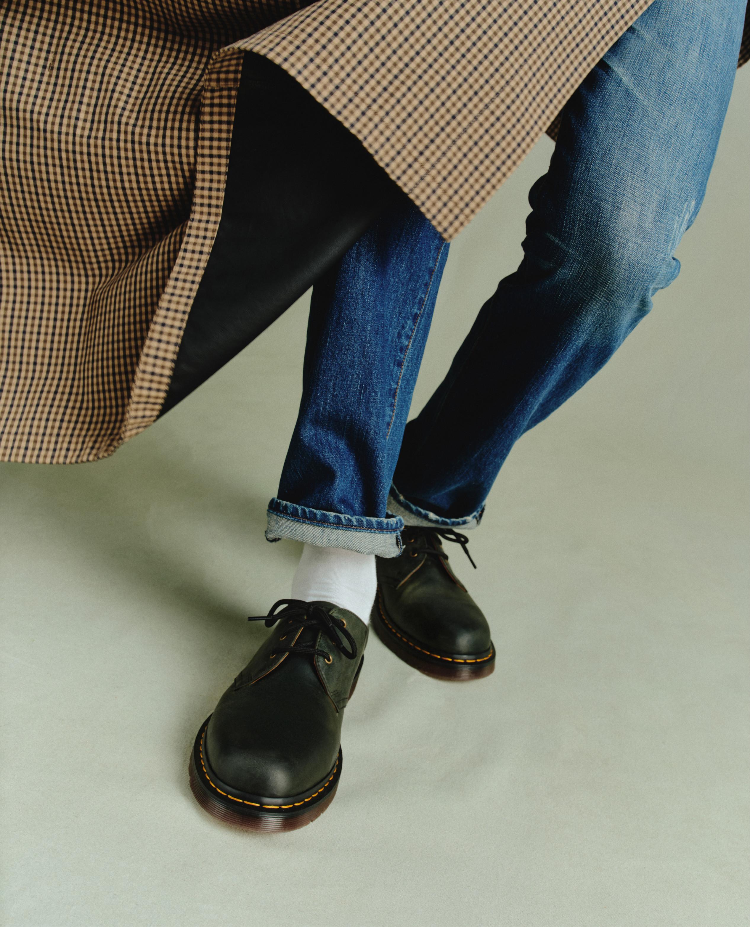 Zapatos negros de piel con cordones y costura amarilla, con vaqueros doblados y calcetines blancos