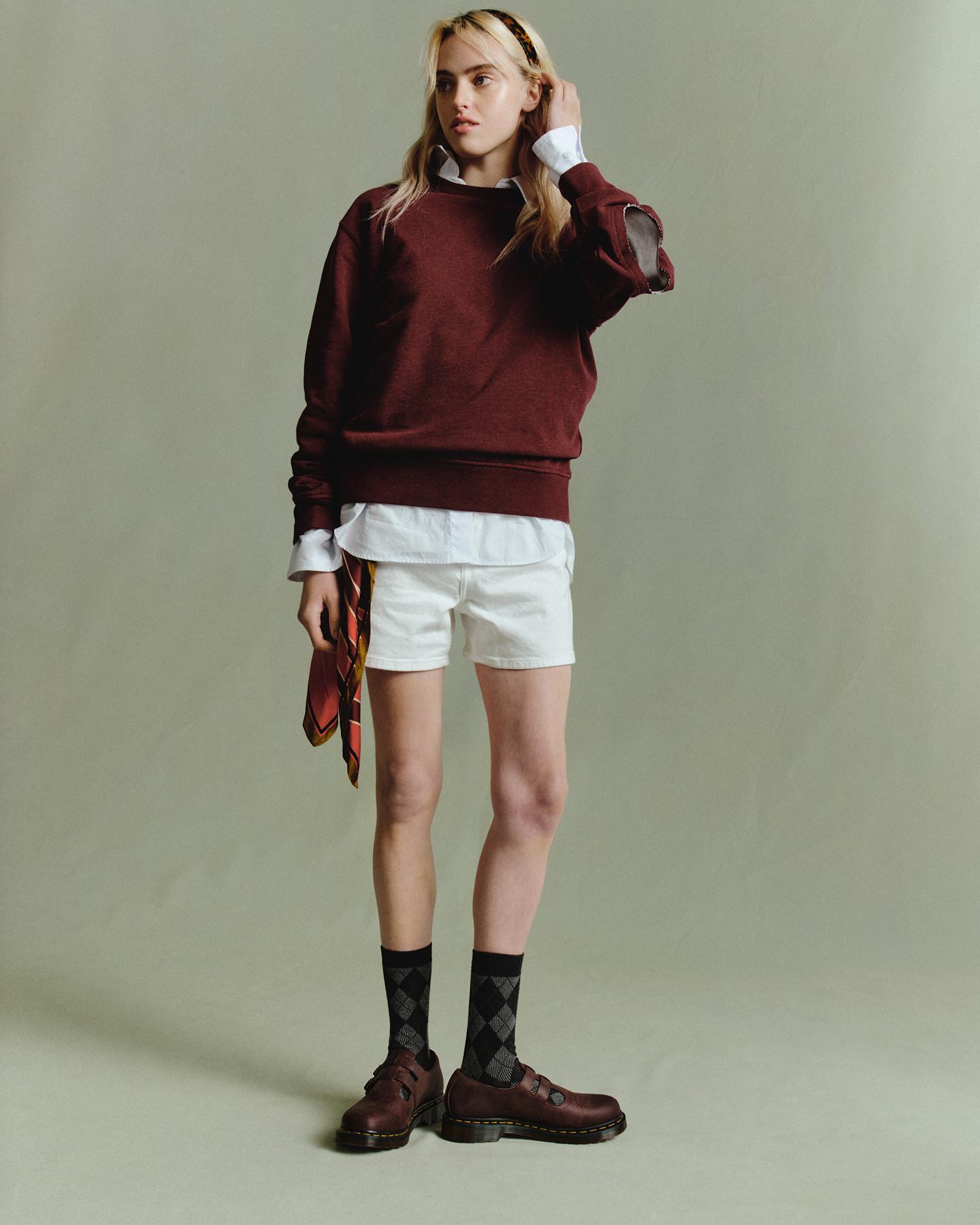 Persona con zapatos de piel rojo cereza, calcetines grises de rombos, shorts blancos y sudadera burdeos