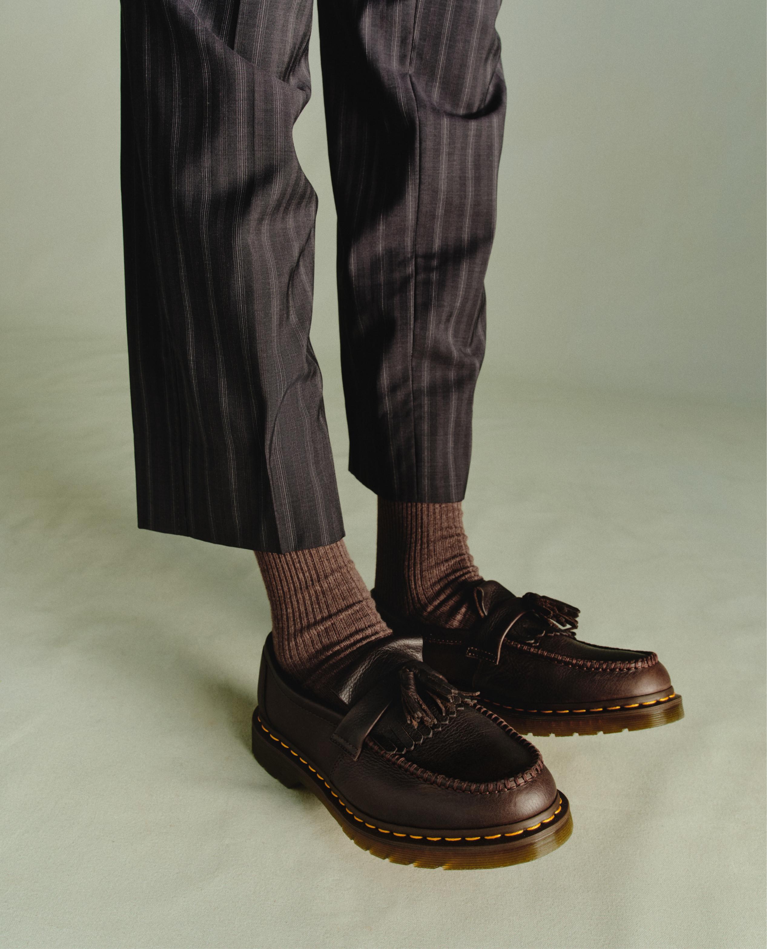Mocasines de piel marrón oscuro con borlas y pespunte amarillo, con pantalón de raya