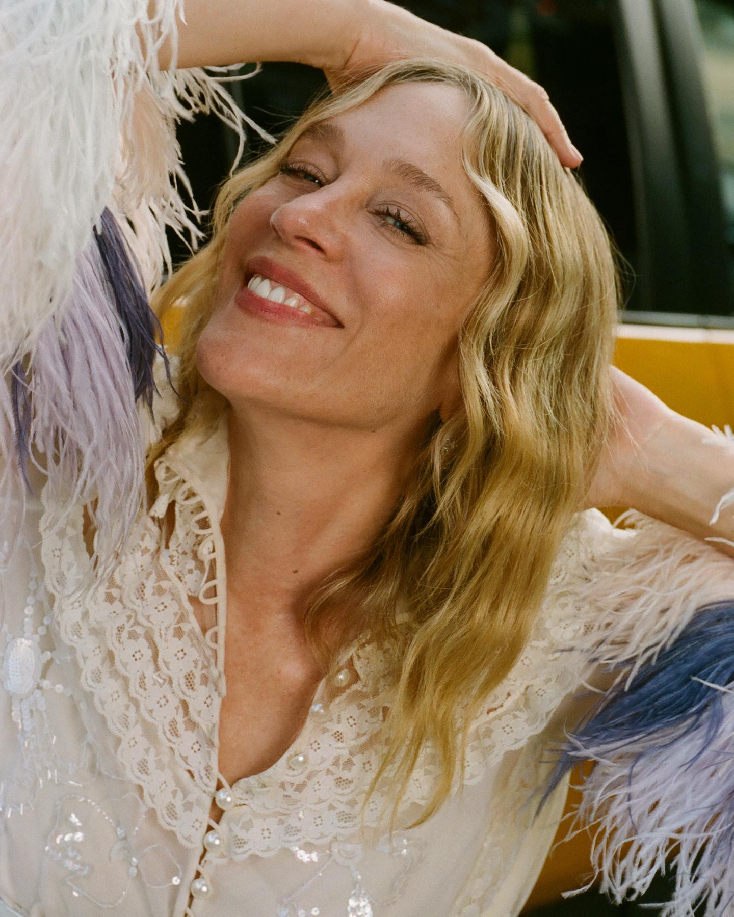 Close-up of a smiling person in a lace blouse with feathered sleeves, leaning back