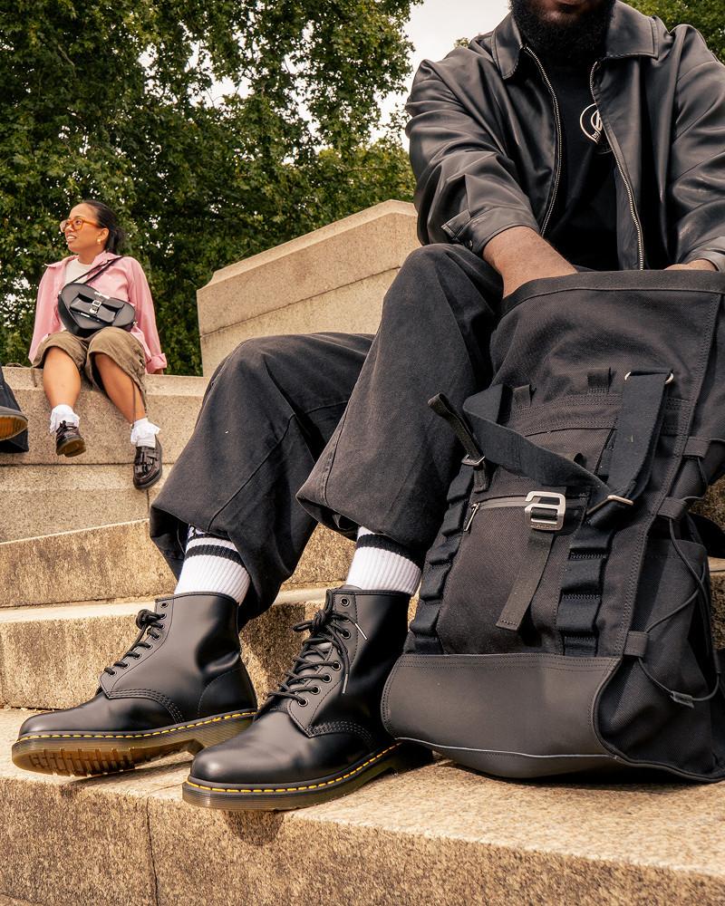 Schwarze Lederstiefel mit Schnürung und gelber Rahmennaht, auf Steinstufen neben schwarzem Rucksack