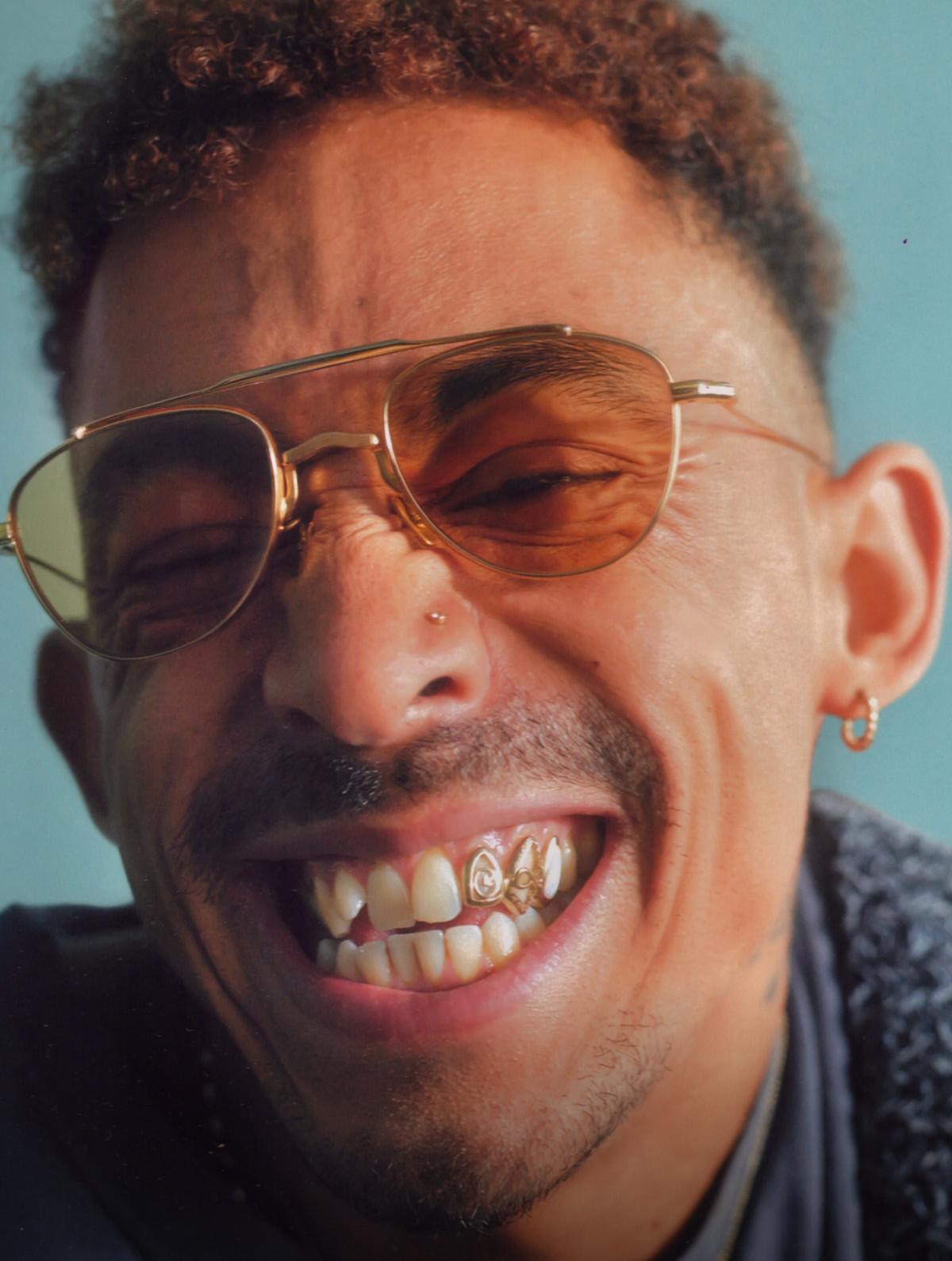 Close-up of a smiling person in gold aviator sunglasses with a gold tooth grill
