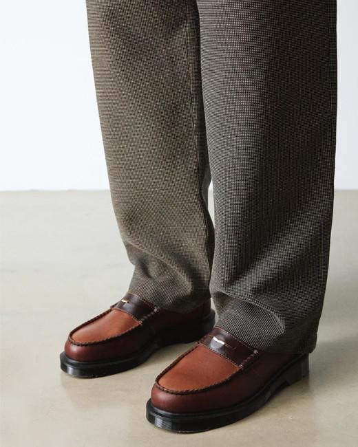 A close up of brown penny loafers with slacks
