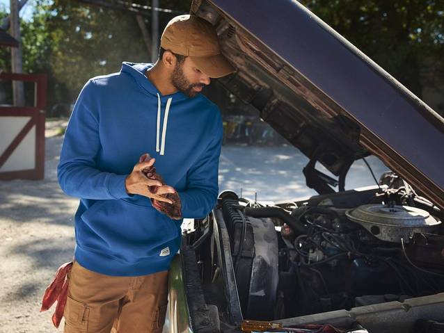 Man wearing a blue hoodie, working under hood of car.