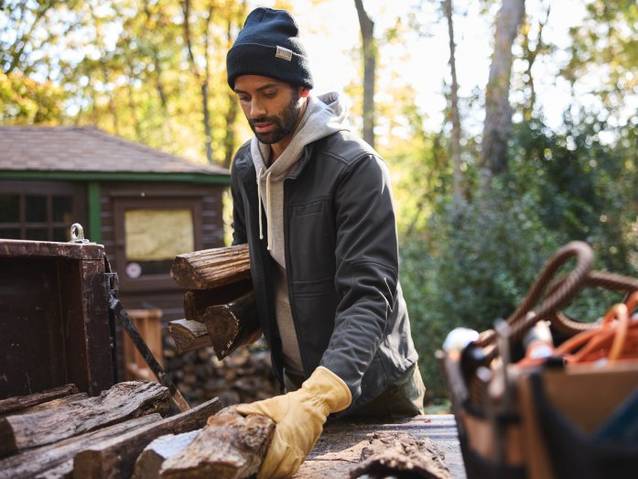 man wearing a hoodie, jacket, beanie and gloves carrying wood 