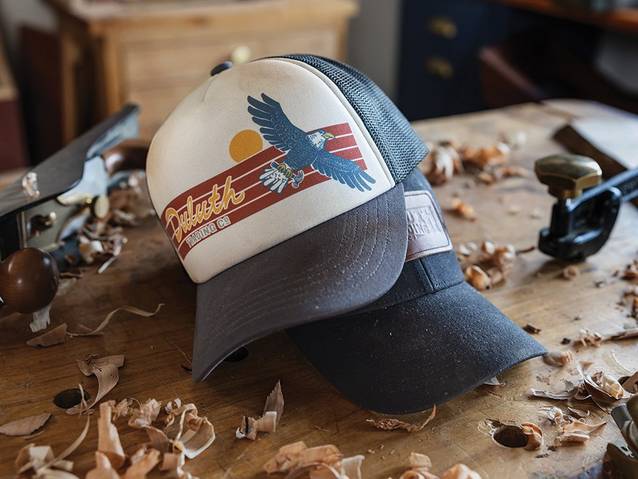 two duluth baseball caps laying on a workbench scattered with wood shavings 