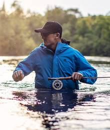 Man fly fishing in river wearing Blue AKHG Olympic Coast jacket