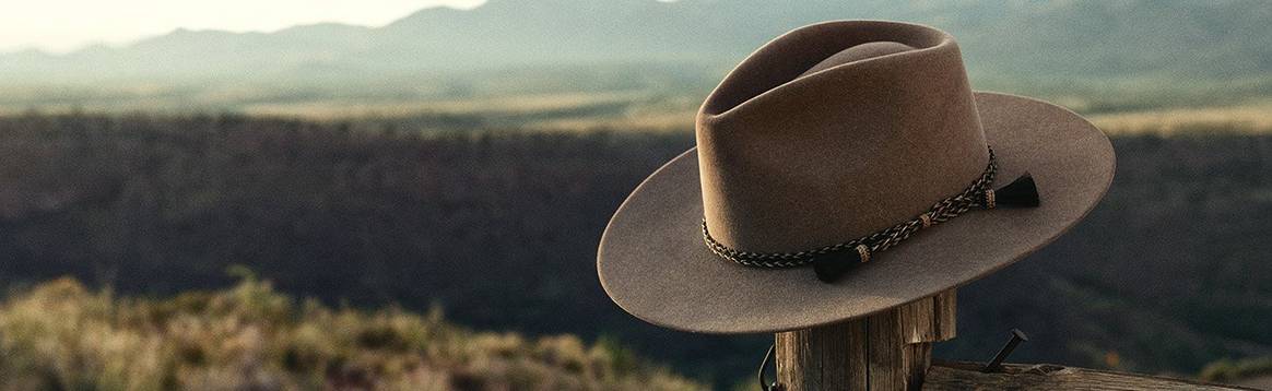 A Stetson hat hangs on an old wooden fence post in front of a serene deset scene