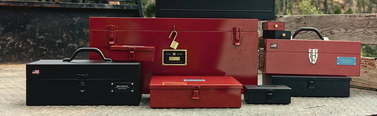 A collection of Best Made steel boxes of all sizes in both black and red sitting in the bed of a rustic pick-up truck