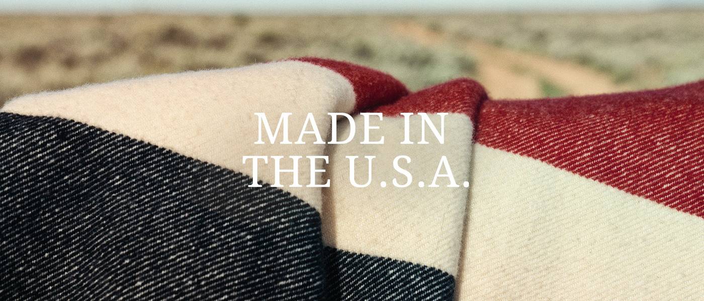 A close up of a red, white and blue woven blanket with a peak of a desert road behind it.