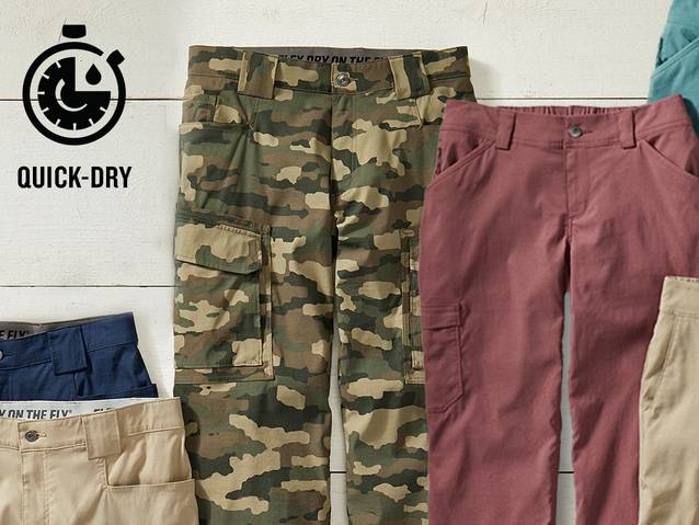 A collection of Dry on the Fly pants in a variety of colors. The main focus is on a men's pair of camoflauge pants and a women's pair of pink pants. There is an icon indicating 'quick-dry' in the corner.