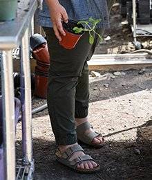 A close up view of green pants on a woman wearing sandals and holding a plant