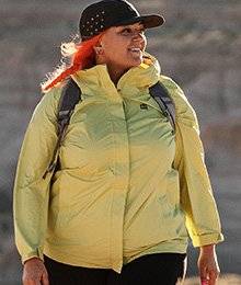 A woman in a yellow jacket wears a backpack and black hat while walking