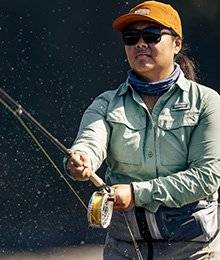 A woman in an orange hat and blue shirt is fly fishing