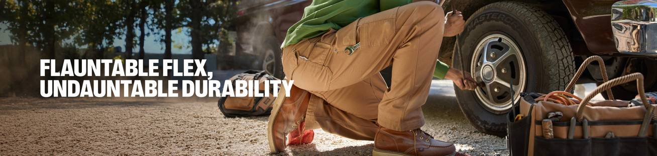 Flauntable flex, undauntable durability. A man in khaki fire hose pants working on a truck tire