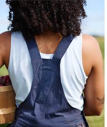 Woman wearing a white tank top under navy blue overalls.