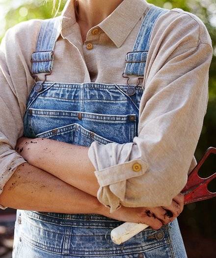 Woman wearing a tan button-down beneath denim overalls.