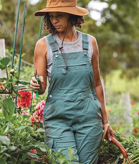 a woman walking in her garden wearing green overalls
