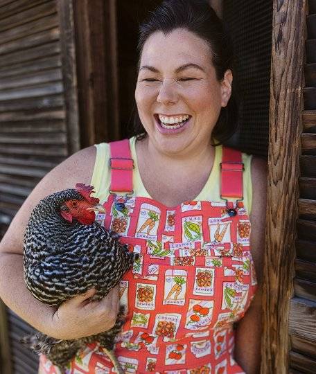 a laughing woman wearing orange overalls holding a chicken