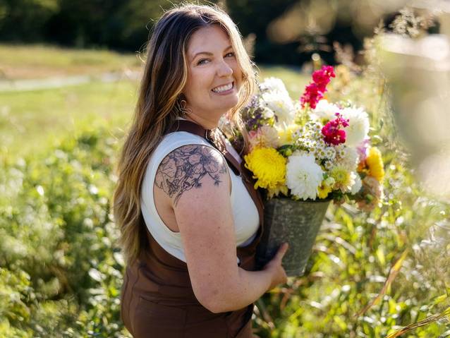 a women wearing brown overalls carrying flowers in a field