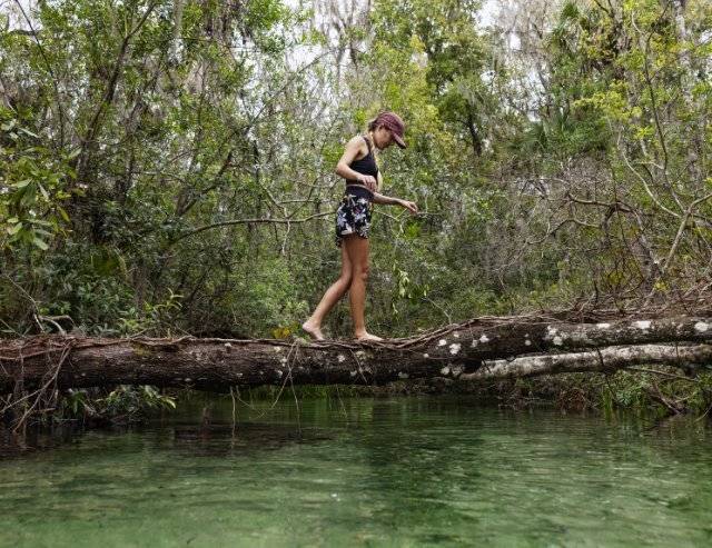 Woman walking on a broken log across a stream in Florida