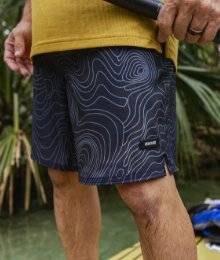 man wearing akhg lost lake swim trunks standing on a paddle board