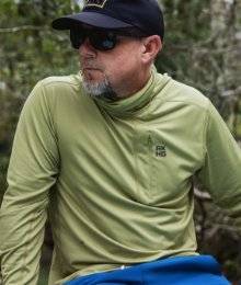 man wearing a green akhg longsleeve sitting on a paddle board looking to the left