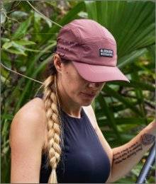 woman wearing mauve akhg hat looking down; standing on a paddle board