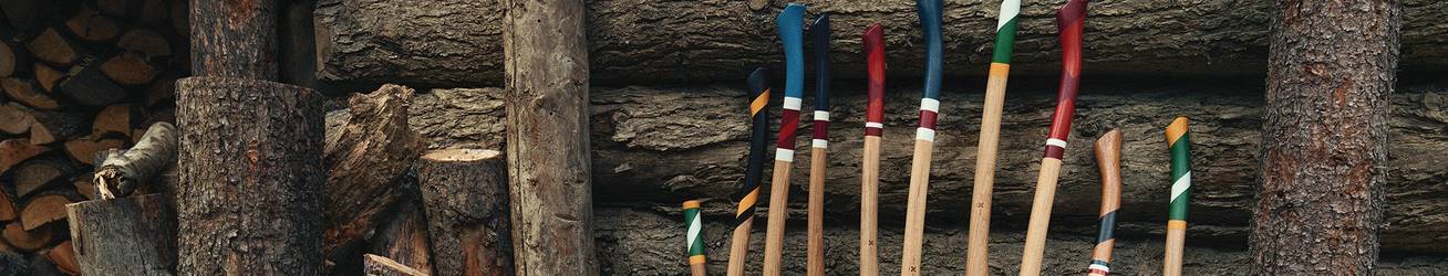 A collection of best made axes sit on a pile of cut wood, leaning against a log cabin