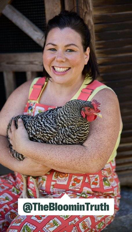 a smiling women wearing coral overalls holding a chicken