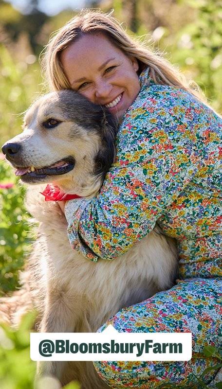 a women wearing multicolored coveralls hugs her fluffy dog