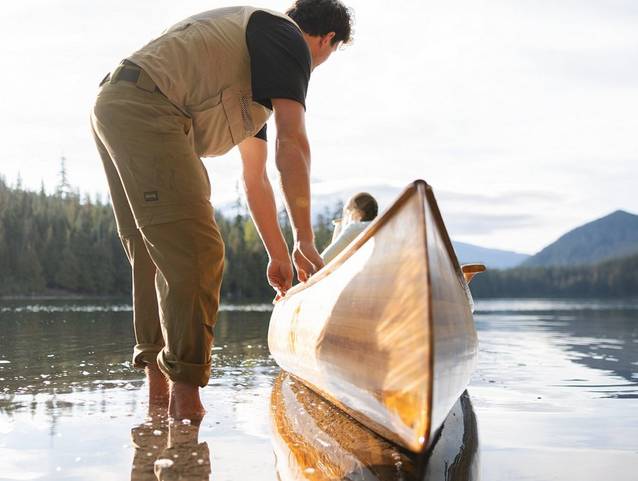 Man wading in shallow water next to canoe.