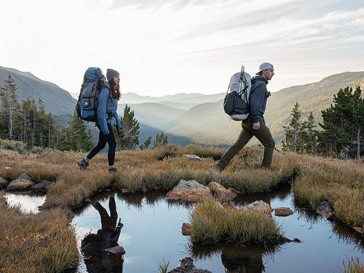 Man and women hiking over a pond in a mountain rainge