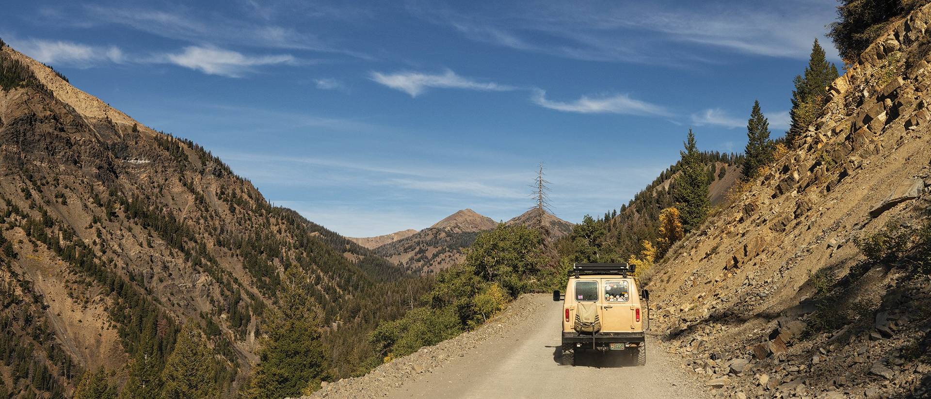 Yellow van driving down dirt road through mountains.