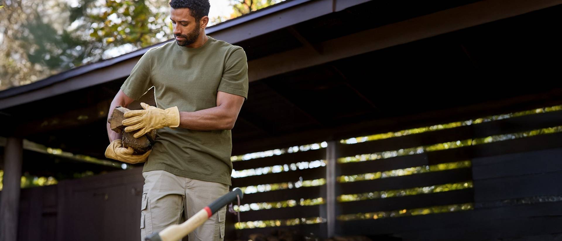 Man wearing green shirt and yellow work gloves carrying wood.