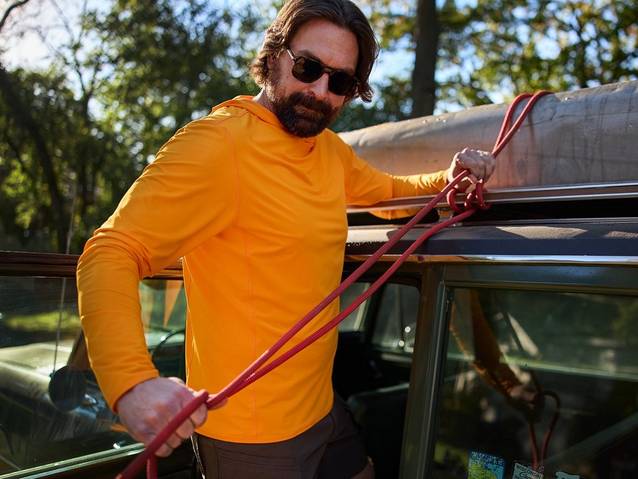 Man in orange shirt strapping canoe to top of car.