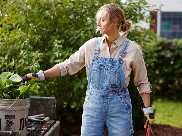 Woman wearing denim overalls, working in garden.