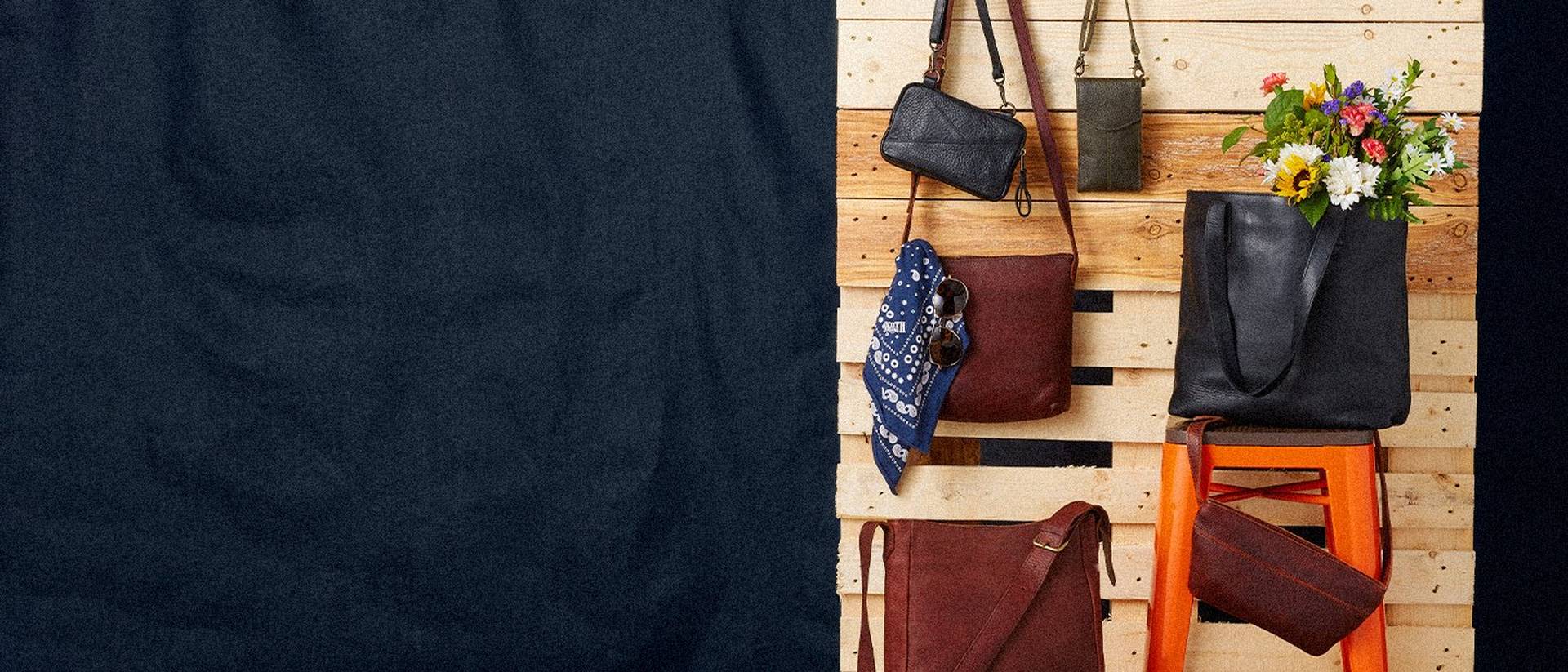 Lifetime Leather bags hanging on a wooden palette wall against a navy linen background