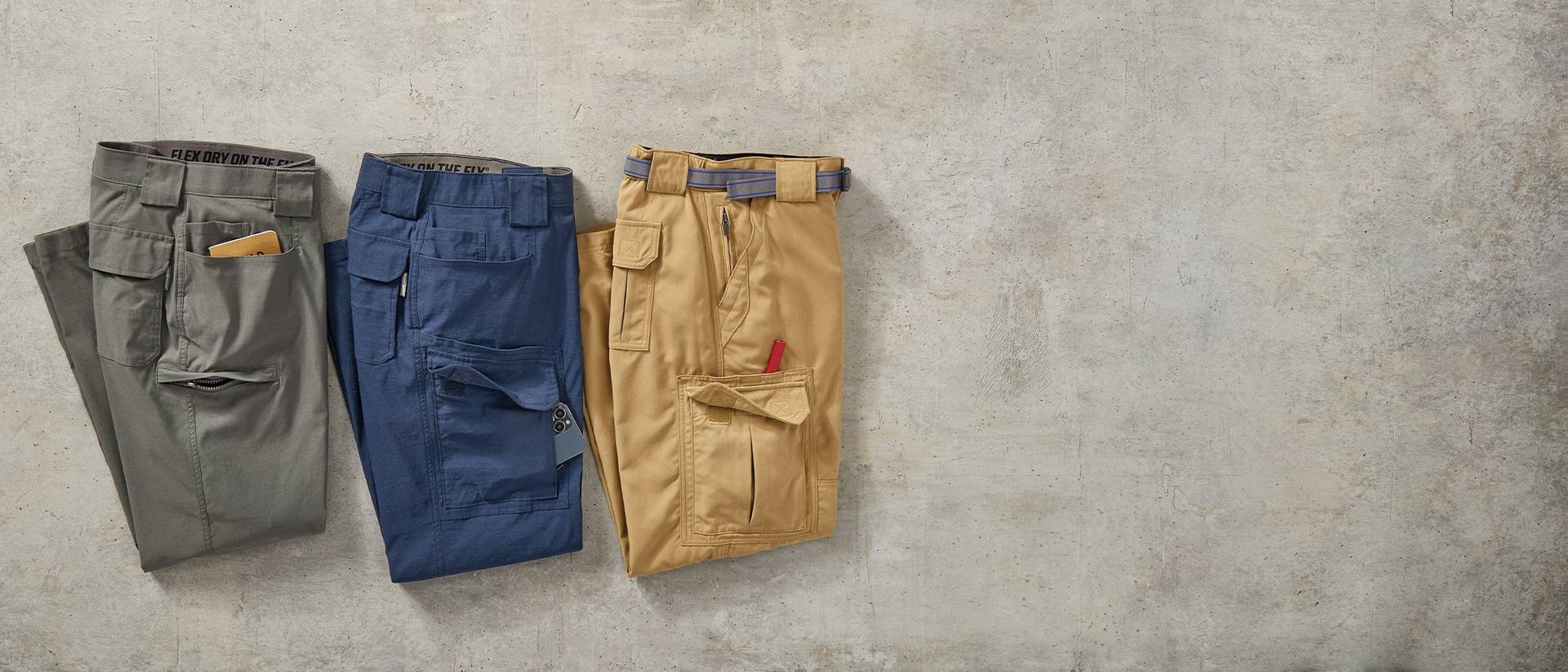 three pairs of men's dry on the fly pants laying on a cement background