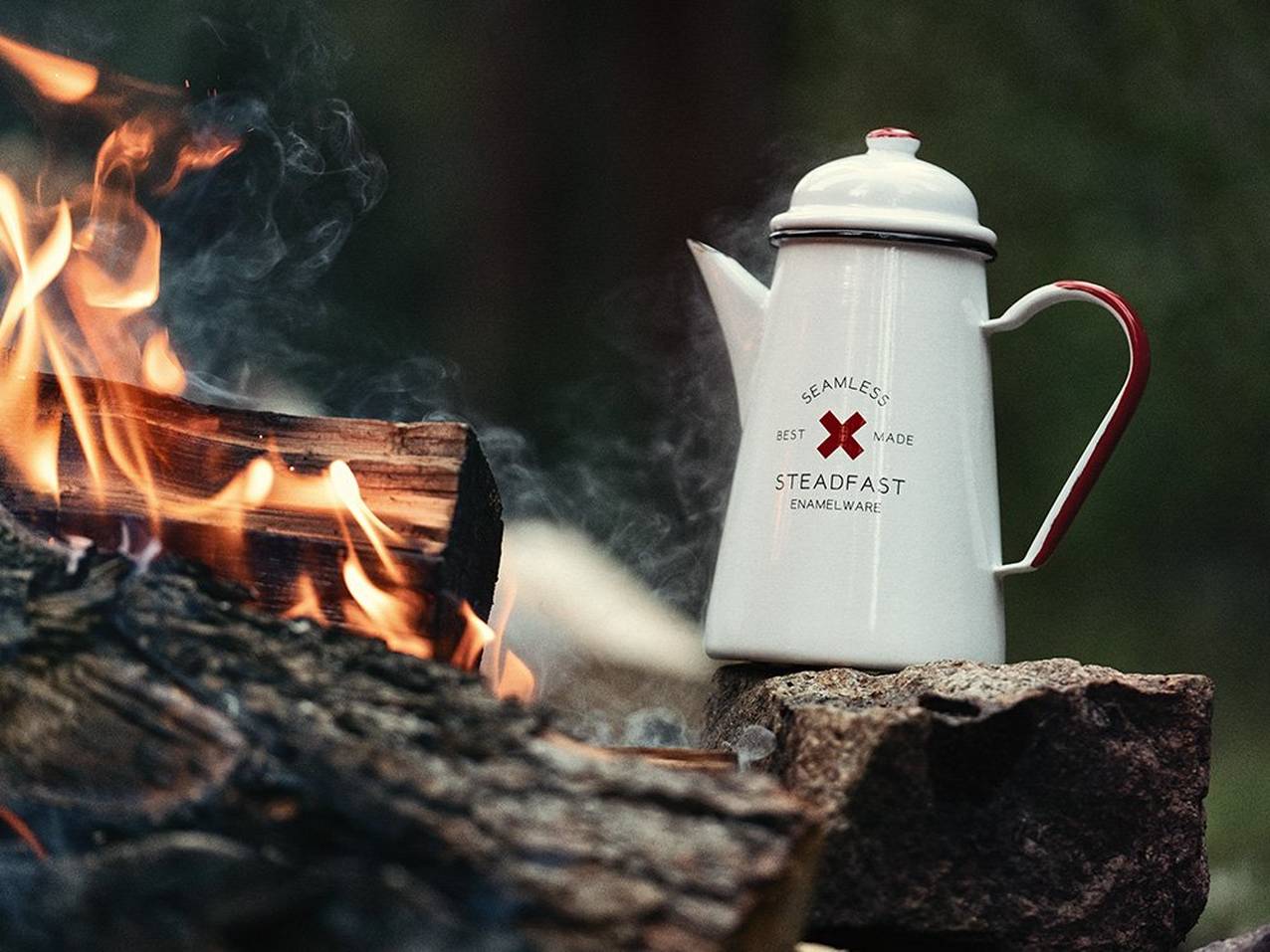 The white Best Made Enamel Cowboy Coffee Kettle sits next to a campfire.