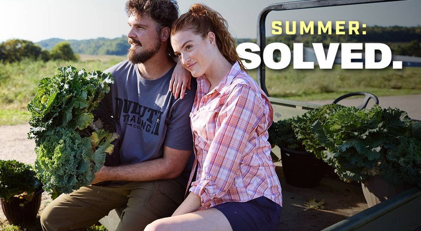 Man and woman sitting in bed of truck, holding lettuce.