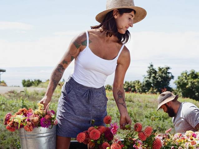 Woman wearing white tank top, carrying buckets of flowers.   