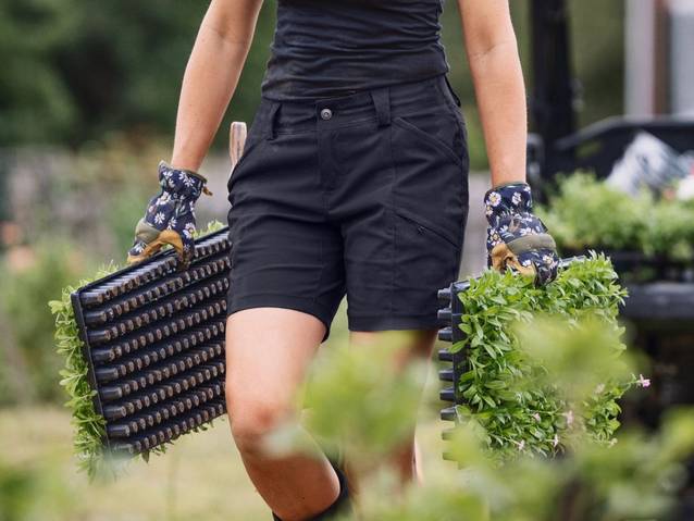 Woman wearing black shorts, carrying plants.