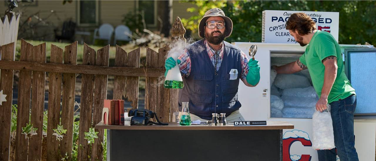 Man holds smoking beaker at table next to man getting ice.