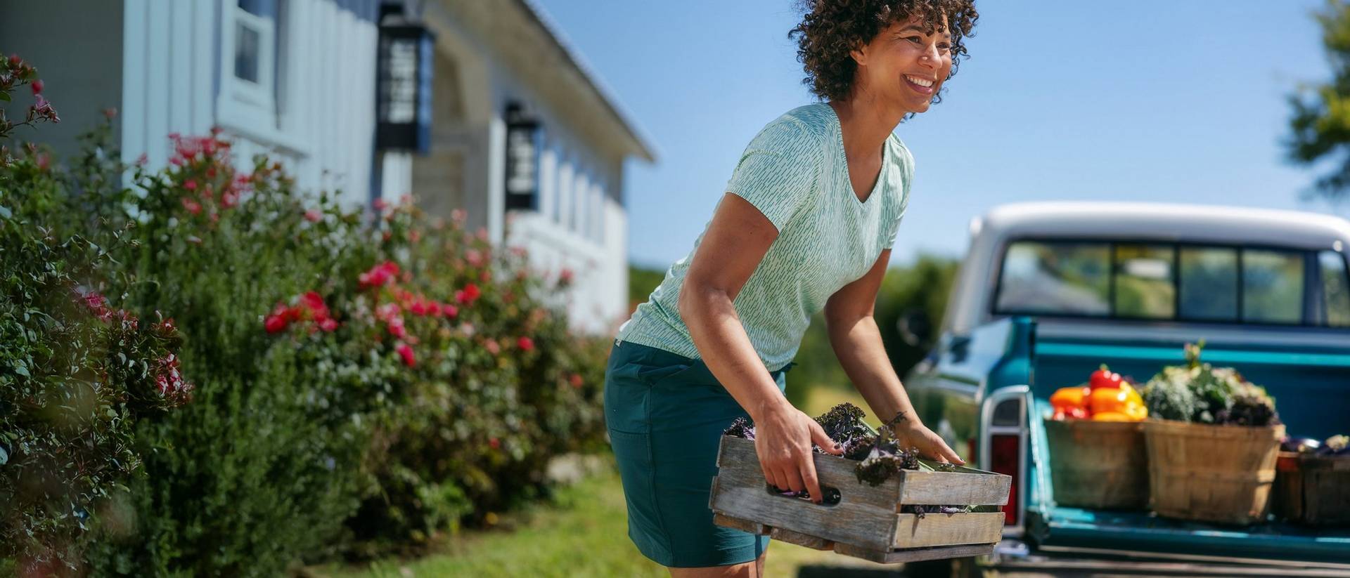 Woman putting baskets of vegetables in the back of a pickup truck.
