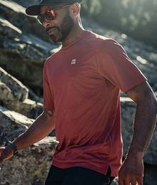 A man in a red shirt in the act of running through a field of large rocks.