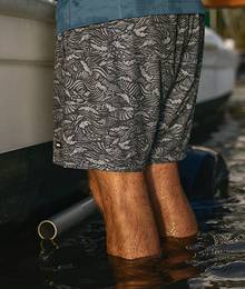 A man in swim trunks stands in water up to his calves.