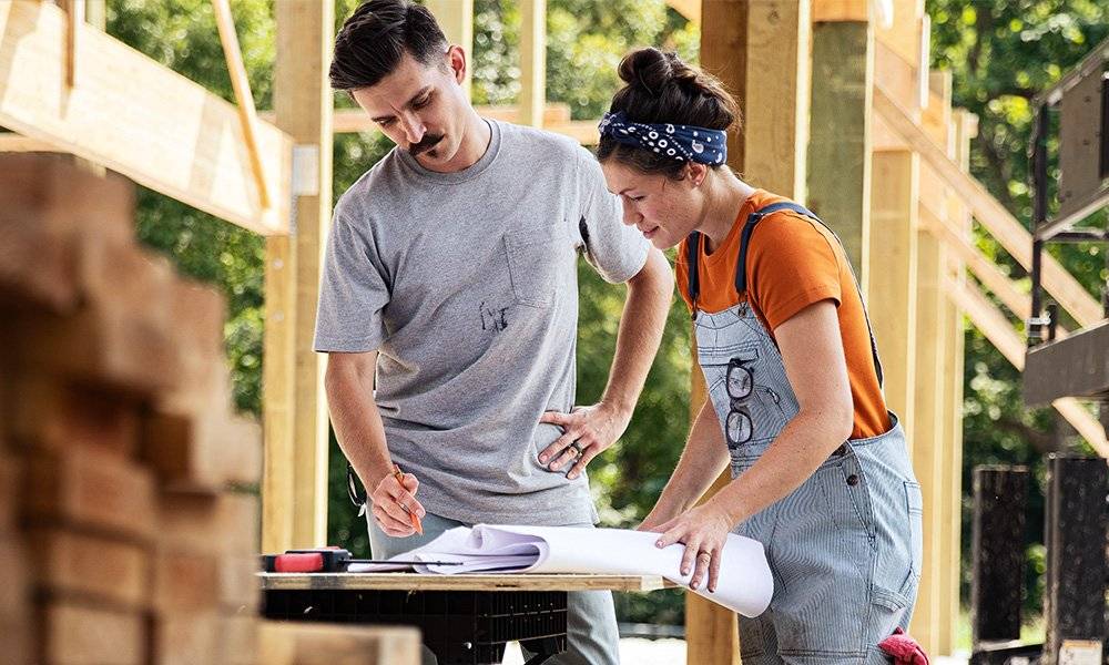 a man and woman review the blueprints for a construction project visible behind them
