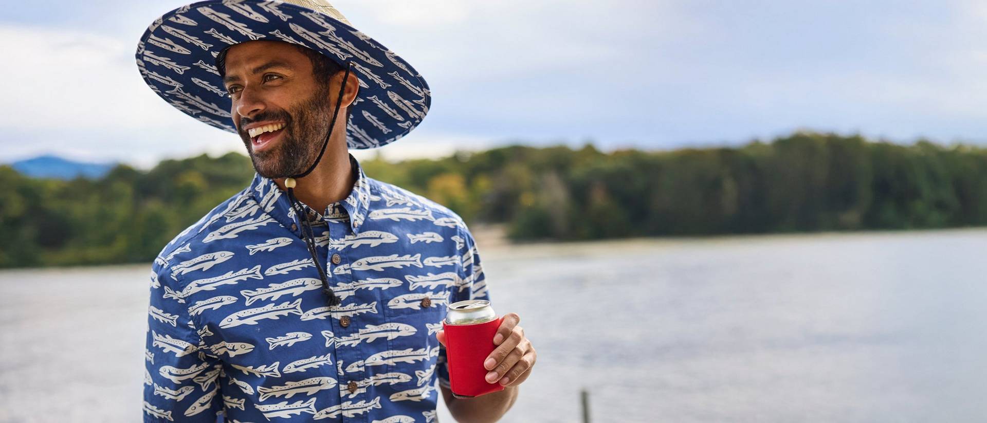 Man wearing a sun hat and button up shirt holding a drink.