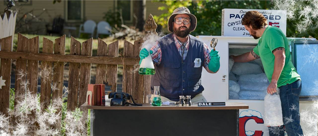 Man holds smoking beaker at table next to man getting ice.